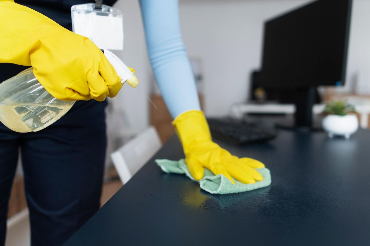 Reinigungskraft wischt einen Schreibtisch mit Mikrofasertuch